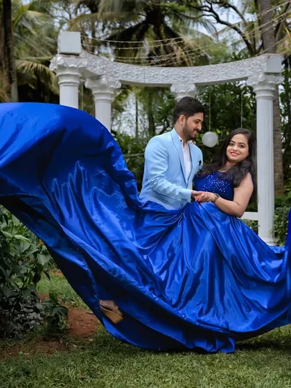 A romantic pose with a flowing blue gown on a swing-like structure in the garden.
