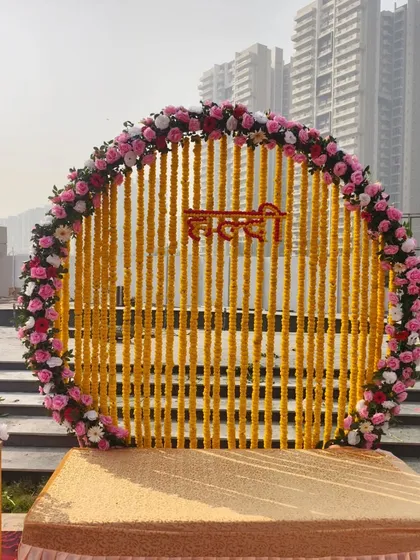 A classic and vibrant Haldi ceremony backdrop. This setup features a circular frame made of marigold (genda) strings and a border of pink and white roses, perfect for traditional pre-wedding functions.