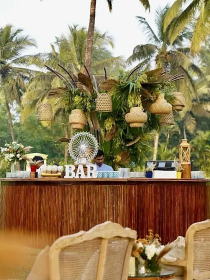 A rustic wooden bar decorated with woven lampshades and tropical leaves for a boho-themed cocktail party in Goa. It's all about creating a relaxed, stylish space for guests to mingle.