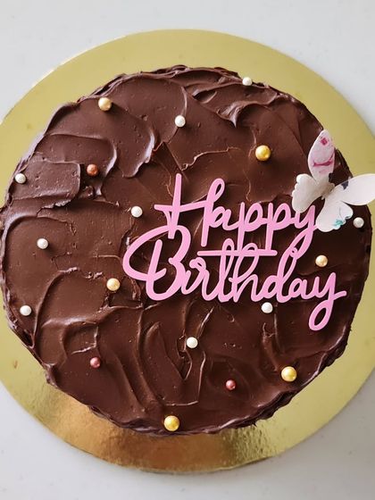 This is an eggless dark chocolate cake filled with fresh strawberries and covered in a rustic ganache. The simple butterfly and "Happy Birthday" topper add a delicate touch to this rich cake.