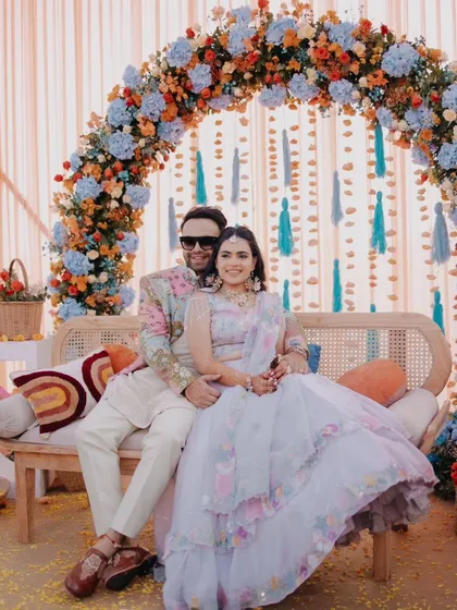 A classic portrait of the couple seated under their colorful Haldi decor, smiling for the camera.