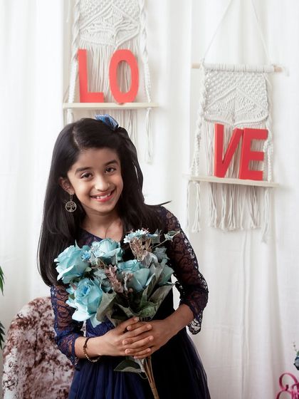 A young girl poses with a bouquet of flowers in my studio. The boho-chic 'LOVE' background adds a sweet and stylish touch to her portrait.