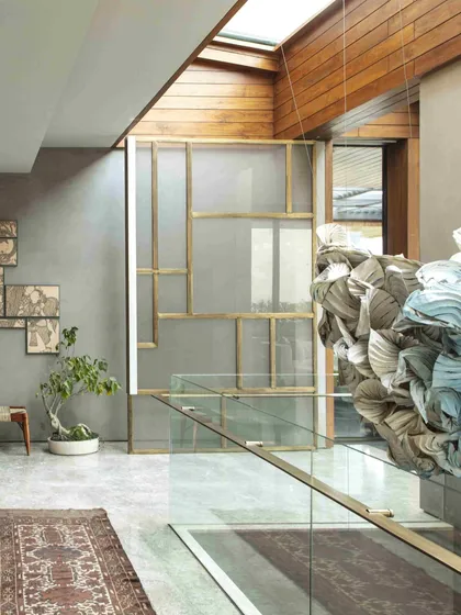 The Shibori and origami installation viewed from the ground floor, looking up through the atrium. The artwork interacts with the home's architecture, including a custom brass and glass screen, creating a layered visual experience.
