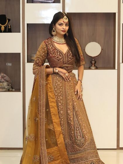 A stunning bridal pose in a golden-beige lehenga with a rich maroon blouse, showcasing the intricate details.