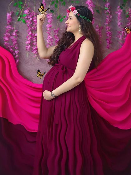 Feeling like a goddess in this whimsical studio setup. The flowing magenta gown, flower crown, and magical butterflies create a truly enchanting maternity portrait.