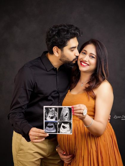 A sweet announcement shot! The couple shares a kiss while holding up their baby's first sonogram pictures, a perfect way to share their joy.