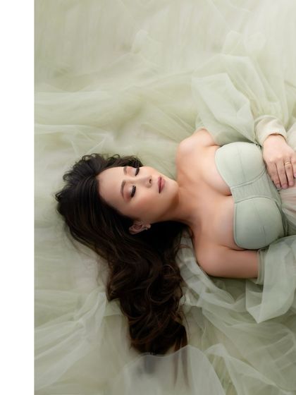 A serene, artistic shot from above. The mother-to-be rests peacefully in a sea of soft green tulle, a portrait of pure tranquility.