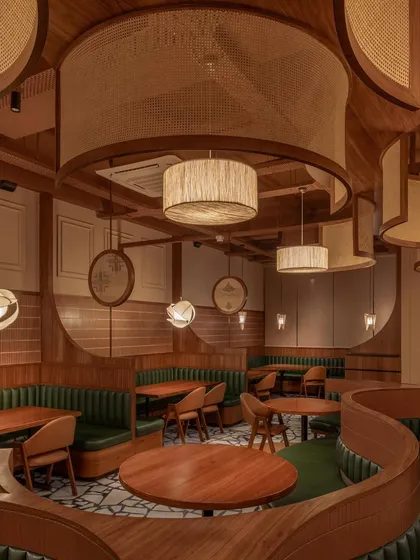 For the Eat Punjab restaurant in Gandhinagar, we designed an immersive dining experience using warm, natural materials. The space is defined by curved, upholstered booth seating in deep green, complemented by custom cane and wood ceiling installations and drum pendants that cast a soft, inviting glow.