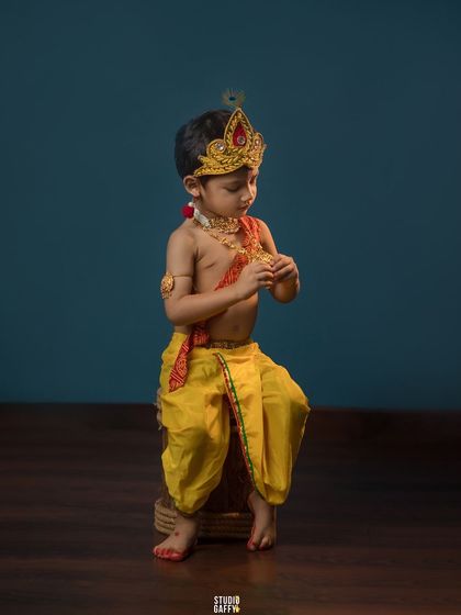 A thoughtful little Krishna, dressed in yellow silk dhoti and a crown.