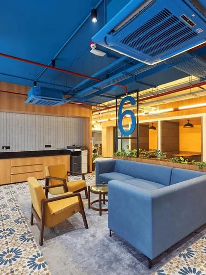 A lounge area with a bold blue ceiling and patterned floor tiles. The space includes a mix of sofas and armchairs, as well as booth seating for more private conversations.