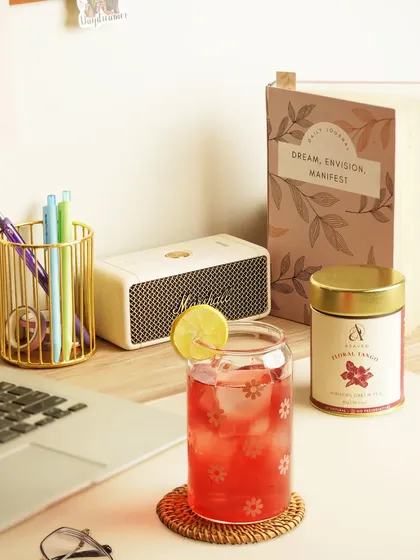 A lifestyle shot of a refreshing red herbal iced tea on a work desk. This image positions the drink as a perfect companion for a productive and pleasant day.