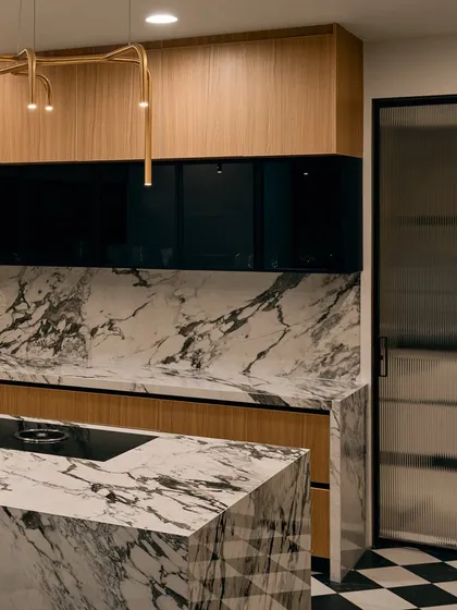 The kitchen island is wrapped entirely in dramatic black and white marble, making it a true statement piece. The modern gold light fixture above adds a touch of elegance.