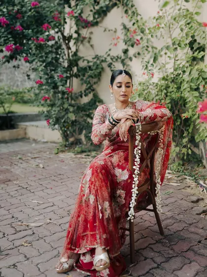 A portrait of the bride seated in a garden, her expression calm and poised. The beautiful floral Sabyasachi saree and the natural setting combine to create an image of timeless elegance.