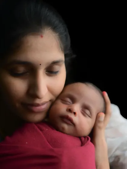 A tender moment between a mother and her newborn. The dark background emphasizes the intimate connection and the soft light on their faces.