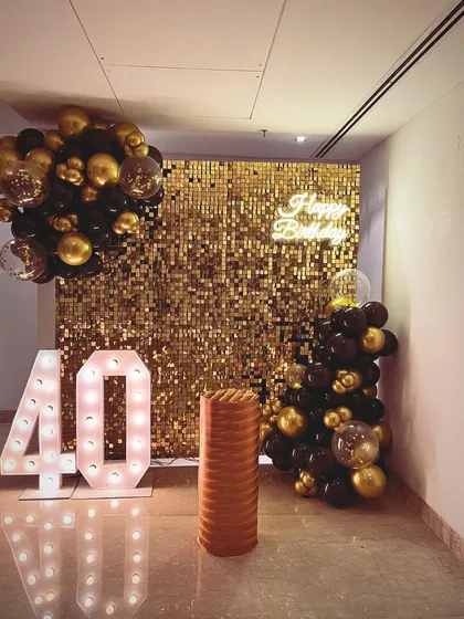 They say life begins at 40, and we agree. This 40th birthday setup in Gurgaon was pure glamour, featuring a gold sequin wall, "Happy Birthday" neon sign, and a classic black and gold balloon arrangement.
