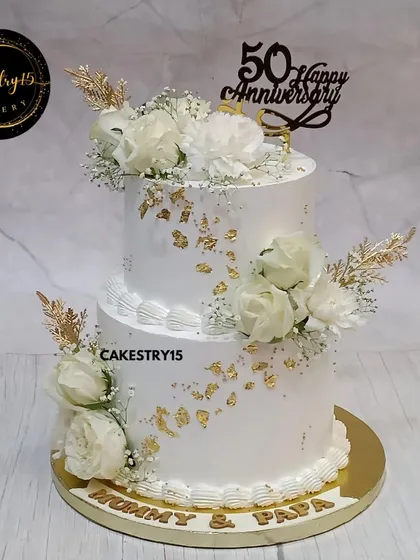 We created this elegant two-tier pineapple cake to honor a beautiful fifty-year love story. It features pristine white frosting, delicate gold leaf accents, and arrangements of fresh white roses, all coming together for a timeless 50th-anniversary centerpiece.