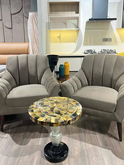 A pair of armchairs in a muted grey fabric with a fan-like, channel-tufted back. The design is subtle yet sophisticated, offering a modern take on a classic silhouette.