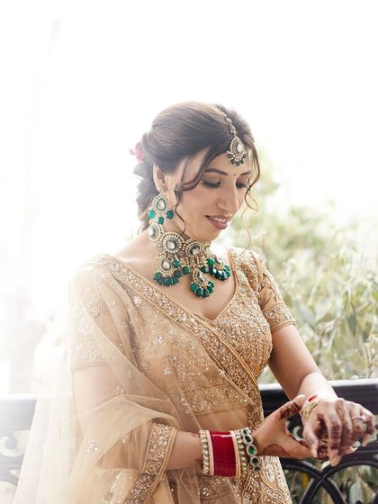 A beautiful portrait of the bride adjusting her bangles. The soft, bright light creates a heavenly glow around her, highlighting her golden lehenga and emerald jewelry.
