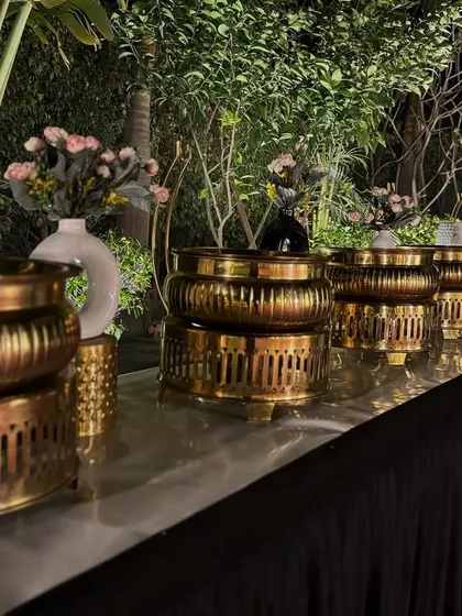 A close-up of our gold chafing dishes with floral arrangements, set up for an evening garden party.