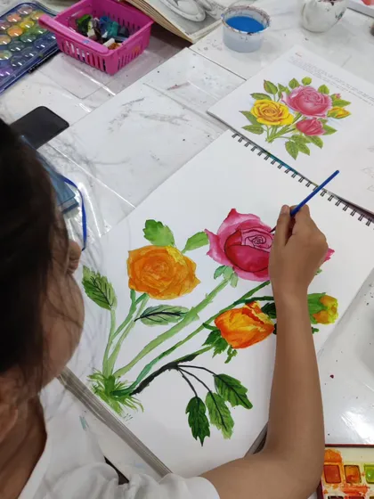 A young student is captured painting a bouquet of roses, learning wet-on-wet and layering techniques in watercolor.