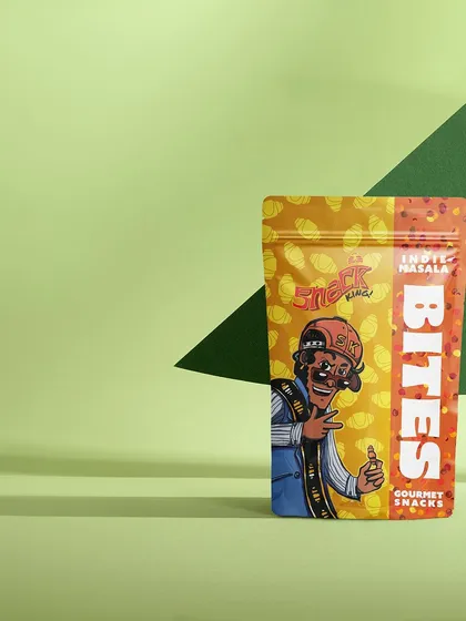 A clean and graphic shot of a snack packet against a two-toned green background. This minimalist, color-blocked style is modern, bold, and makes the colorful packaging stand out.