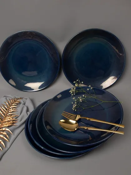 An elegant tabletop arrangement of deep blue ceramic dinner plates, styled with golden cutlery and delicate flowers to create a sophisticated dining aesthetic.