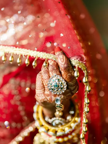 A detailed shot of the bride's hand, showcasing her beautiful ring and henna design against the rich fabric of her wedding dress.