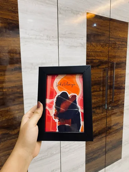 A still image of the pop out couple frame, held against a wooden background. This shot clearly shows the 3D effect and the vibrant colors of the illustration.