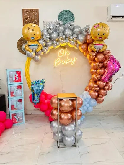 A modern and colorful 'Oh Baby' setup. The circular arch is decorated with balloons in four different colors, with large baby and foot-shaped foil balloons for a playful touch.