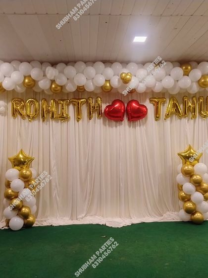 A simple and sweet engagement or wedding stage with a white curtain backdrop and gold and white balloon pillars.