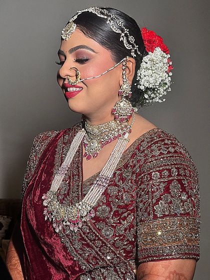 A happy bride in a stunning maroon velvet lehenga. The look is completed with a beautiful floral bun and a radiant smile.