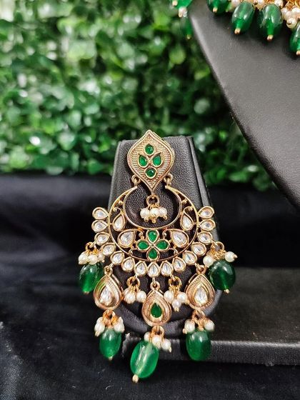 The matching earring for this set, featuring the same kundan work and green bead drops.