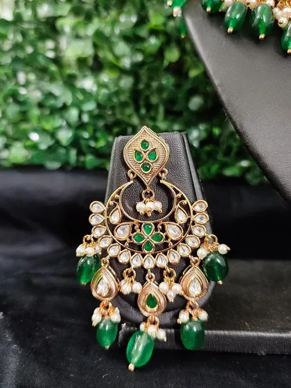 The matching earring for this set, featuring the same kundan work and green bead drops.