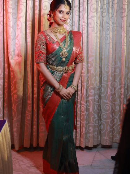 A full-length view of a classic South Indian bridal look. The rich green and red Kanjivaram saree is perfectly draped to create a slim, elegant silhouette.