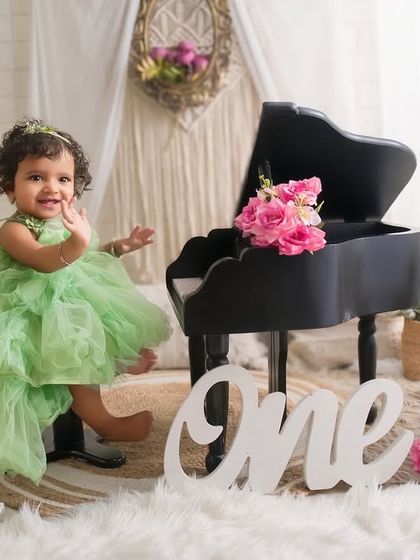 Waving hello to being one year old. This adorable shot captures the happy and playful spirit of a first birthday girl in her beautiful green dress.