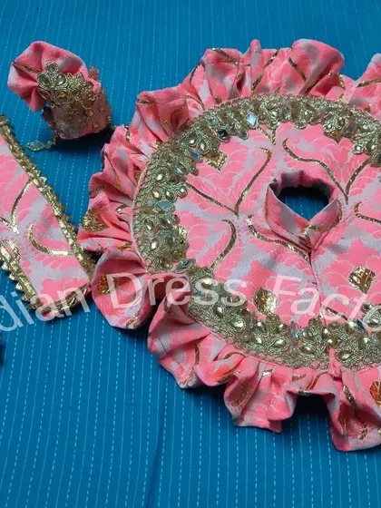 This is another custom-stitched poshak for Laddu Gopal, featuring a pink and gold brocade fabric with delicate mirror work along the border. The set includes a matching dress, pants, and mukut.