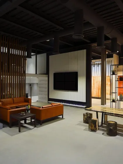 A lounge area within the showroom, featuring a mix of rustic and modern furniture. The space is defined by wooden partitions and a large media screen, creating a comfortable spot for client consultations.