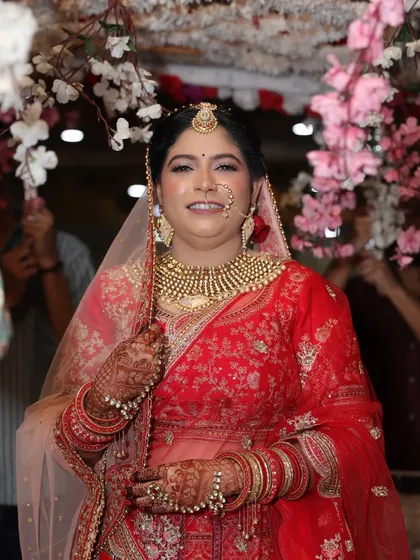 A beautiful bride framed by cherry blossoms. Her classic red lehenga and gold jewelry are perfectly complemented by a soft, glowing makeup look.