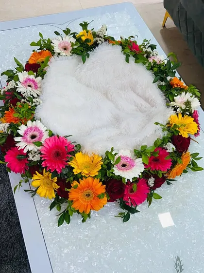 A beautiful and soft cradle for the baby, surrounded by a wreath of fresh, vibrant gerbera daisies.