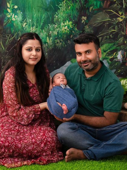 A family sits together against a lush, jungle-themed backdrop, holding their newborn. This image shows how we can incorporate creative themes into family portraits for a unique and memorable result.