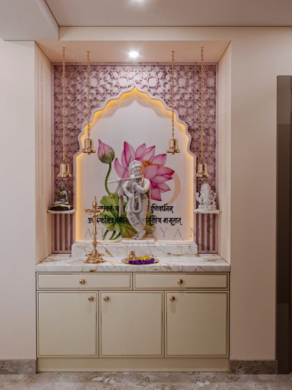 A beautiful mandir design featuring a floral inlay backdrop, hanging brass bells, and a clean, off-white cabinet for storage.