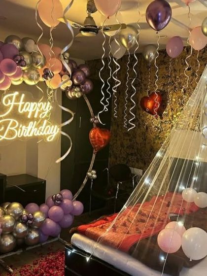 A beautiful room decoration in shades of purple, pink, and silver. This setup includes a balloon semi-arch, balloons on the ceiling, and a fairy light canopy over the bed.