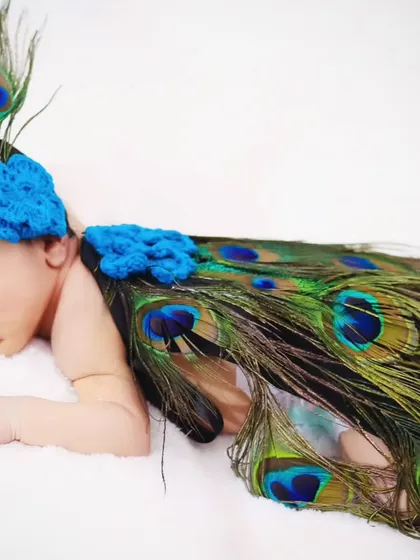 A creative newborn photoshoot featuring a unique peacock theme. The baby is adorned with soft peacock feathers for a touch of vibrant color and imagination.