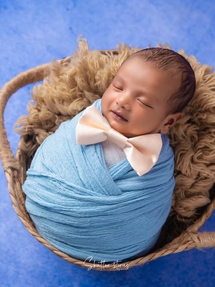 A sweet sleeping face with a gentle smile, this newborn looks dapper in his blue swaddle and bow tie.