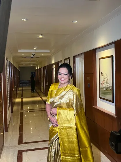 The mother of the groom, looking radiant in a stunning gold saree. Her makeup is classic and elegant, with a traditional red bindi to complete the look.