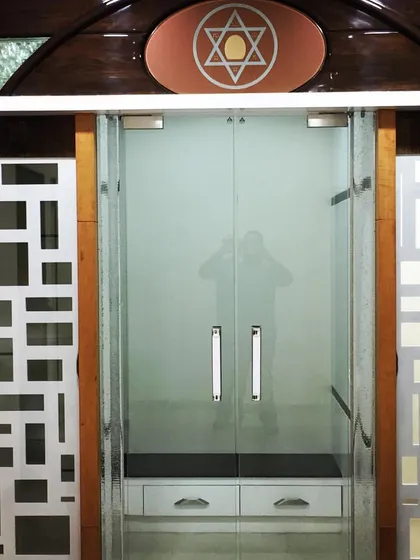 The entrance to this pooja room features frosted glass doors for privacy, flanked by decorative panels with modern geometric cutouts. This blends traditional function with contemporary design.