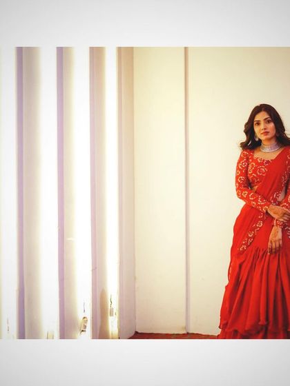 A full shot of the client in her red ruffled lehenga saree, showcasing the complete look against a simple backdrop.