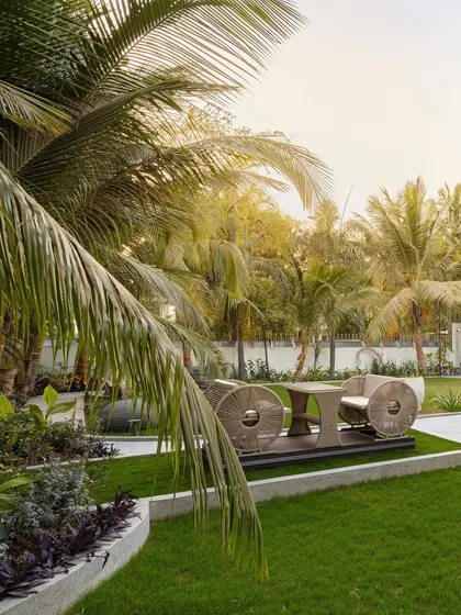 A dedicated seating nook at 'Tropical Manor', elevated slightly above the lawn. This space, framed by lush palm fronds, offers a private spot to enjoy the garden's serenity and the unique design of the outdoor furniture.