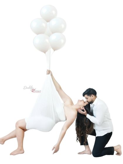 A creative and romantic couple's portrait. The mom-to-be is suspended gracefully with balloons while her partner kneels beside her, creating a magical and unique photo.