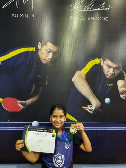 Another shot of Varya with her gold medal and certificate from the district tournament. She stands in front of a poster of table tennis legends, a true inspiration for our future champs.
